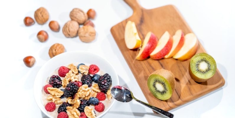 A nutritious breakfast bowl featuring fresh berries and walnuts, served with sliced fruit and kiwi.