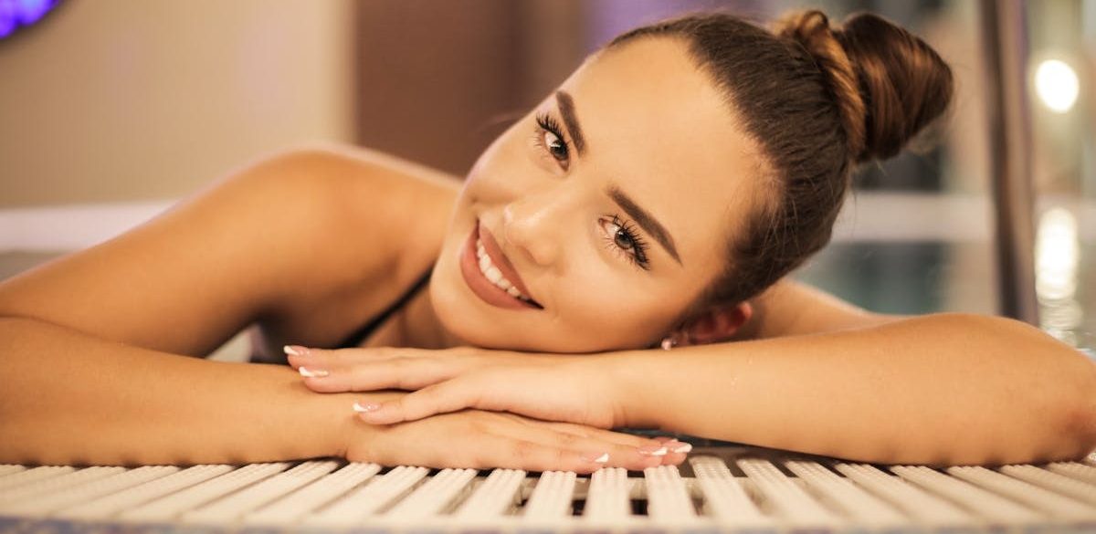 A happy woman with a bun relaxing and smiling at an indoor poolside, creating a warm and inviting atmosphere.