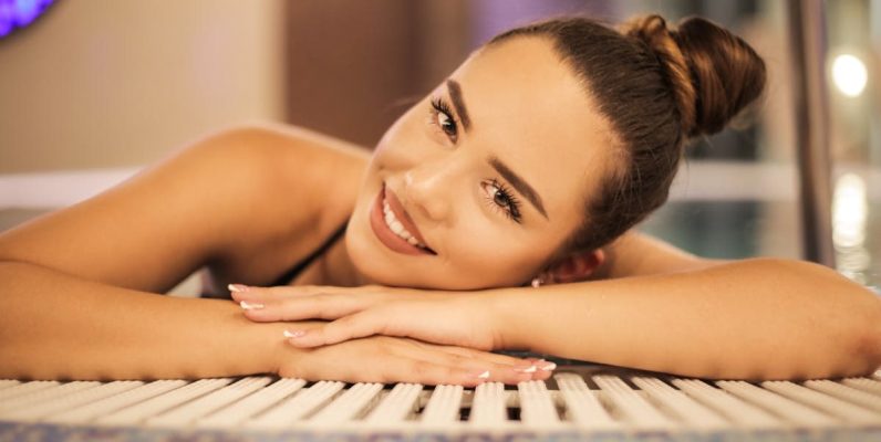 A happy woman with a bun relaxing and smiling at an indoor poolside, creating a warm and inviting atmosphere.